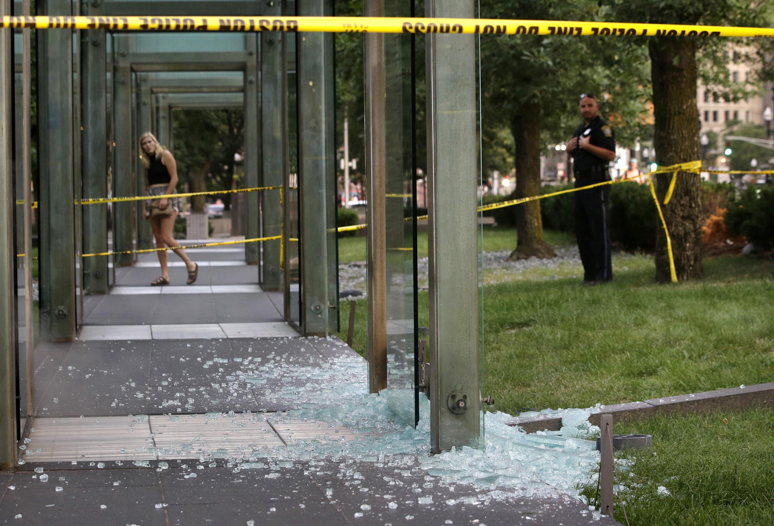A passerby, left, and a law enforcement official, right, stand near broken glass at the New England Holocaust Memorial