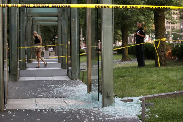 A passerby, left, and a law enforcement official, right, stand near broken glass at the New England Holocaust Memorial