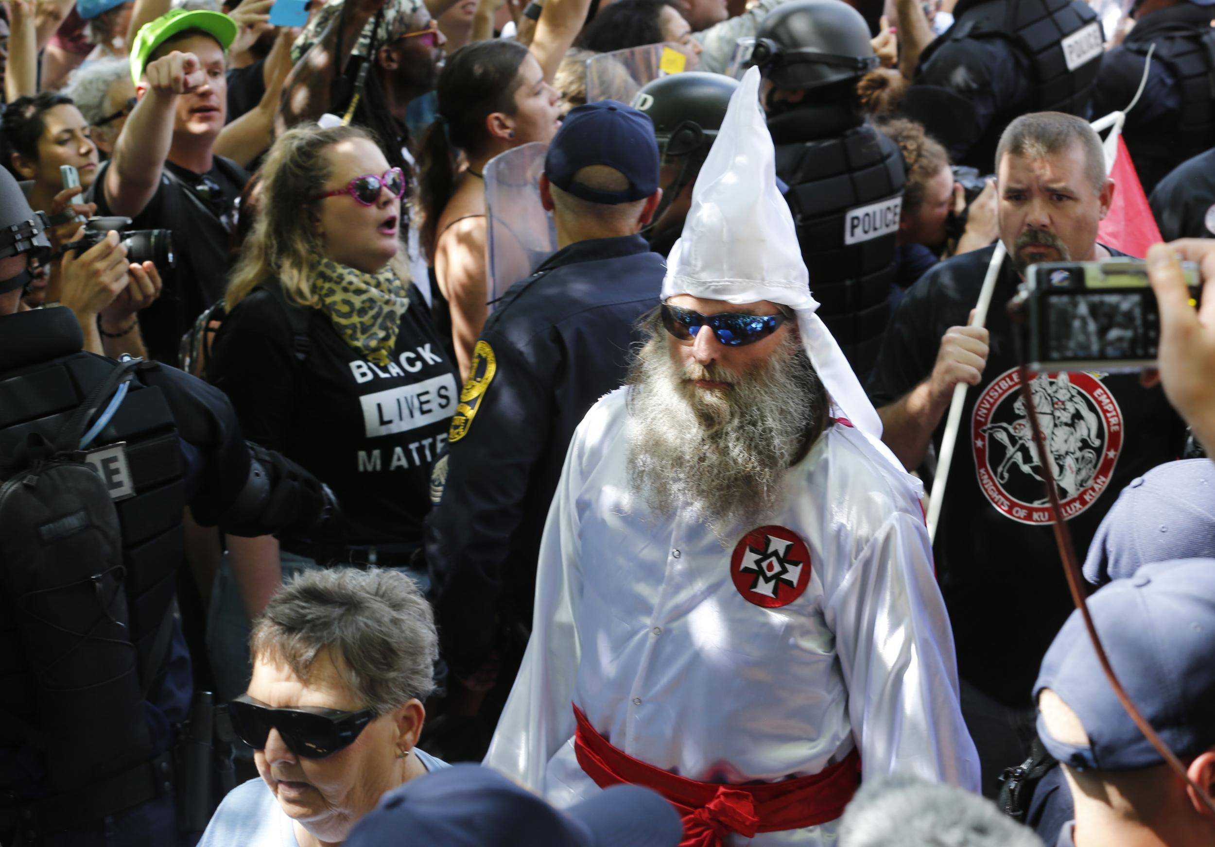 Members of the KKK are escorted by police past a large group of protesters during a rally in Charlottesville (AP)