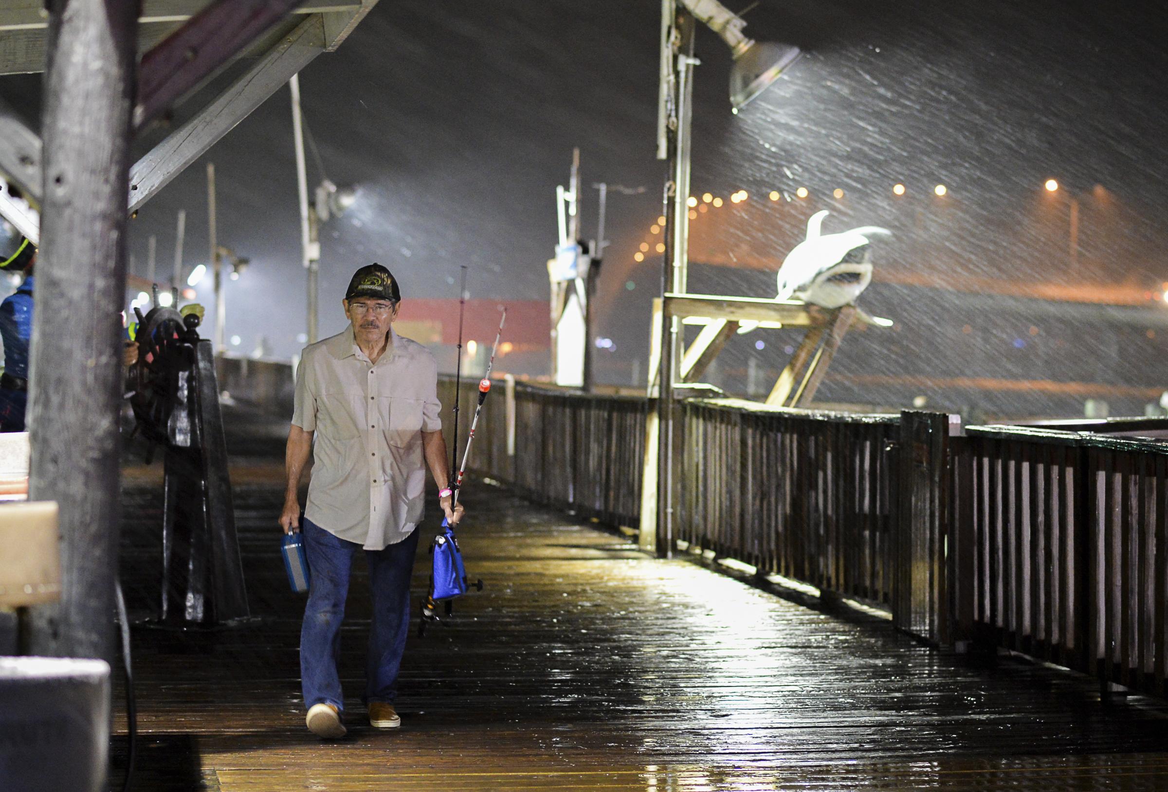 Rogelio Ortiz makes his way off the Pirate's Landing Fishing Pier as rain from Hurricane Harvey falls