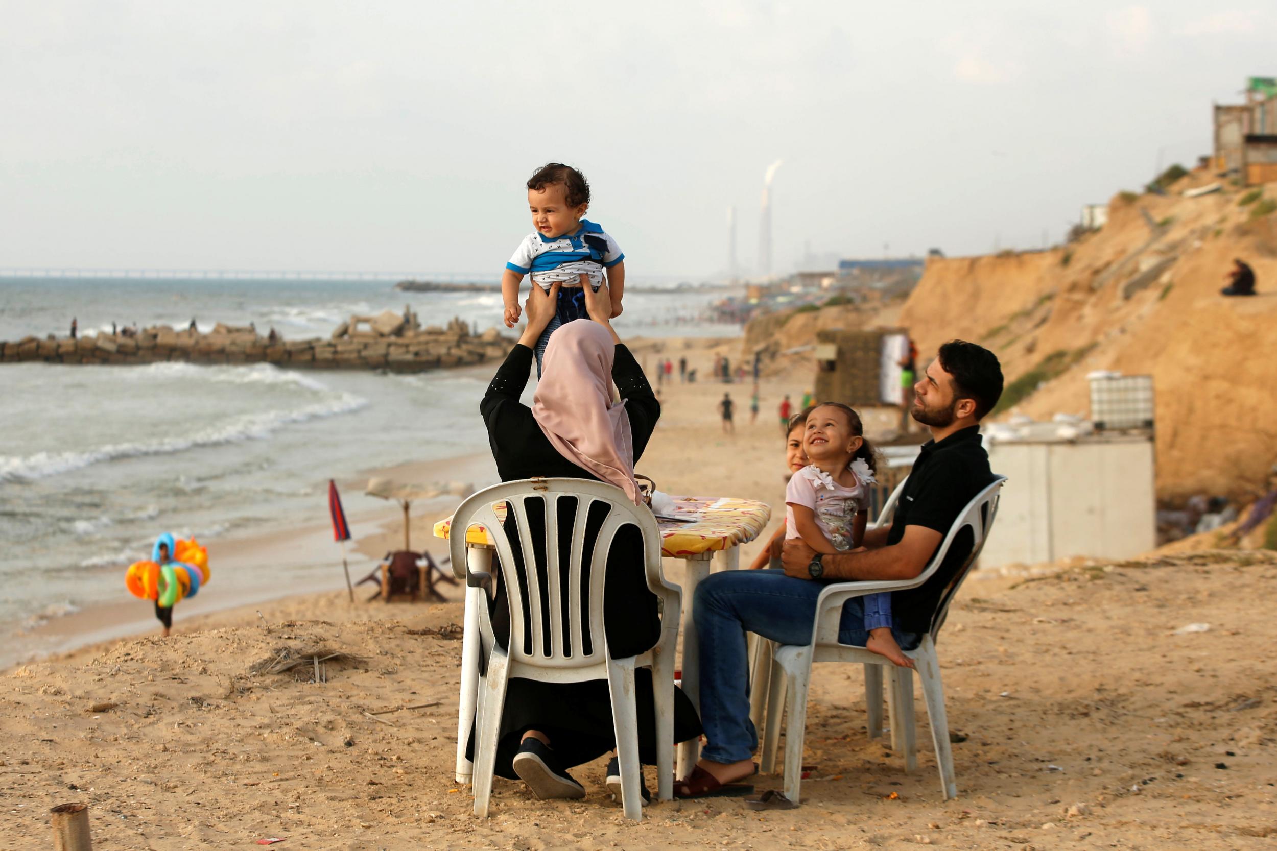 A woman lifts up her son as she sits with her family on a beach in Beit Lahiya town in the northern Gaza Strip on 6 July 2017