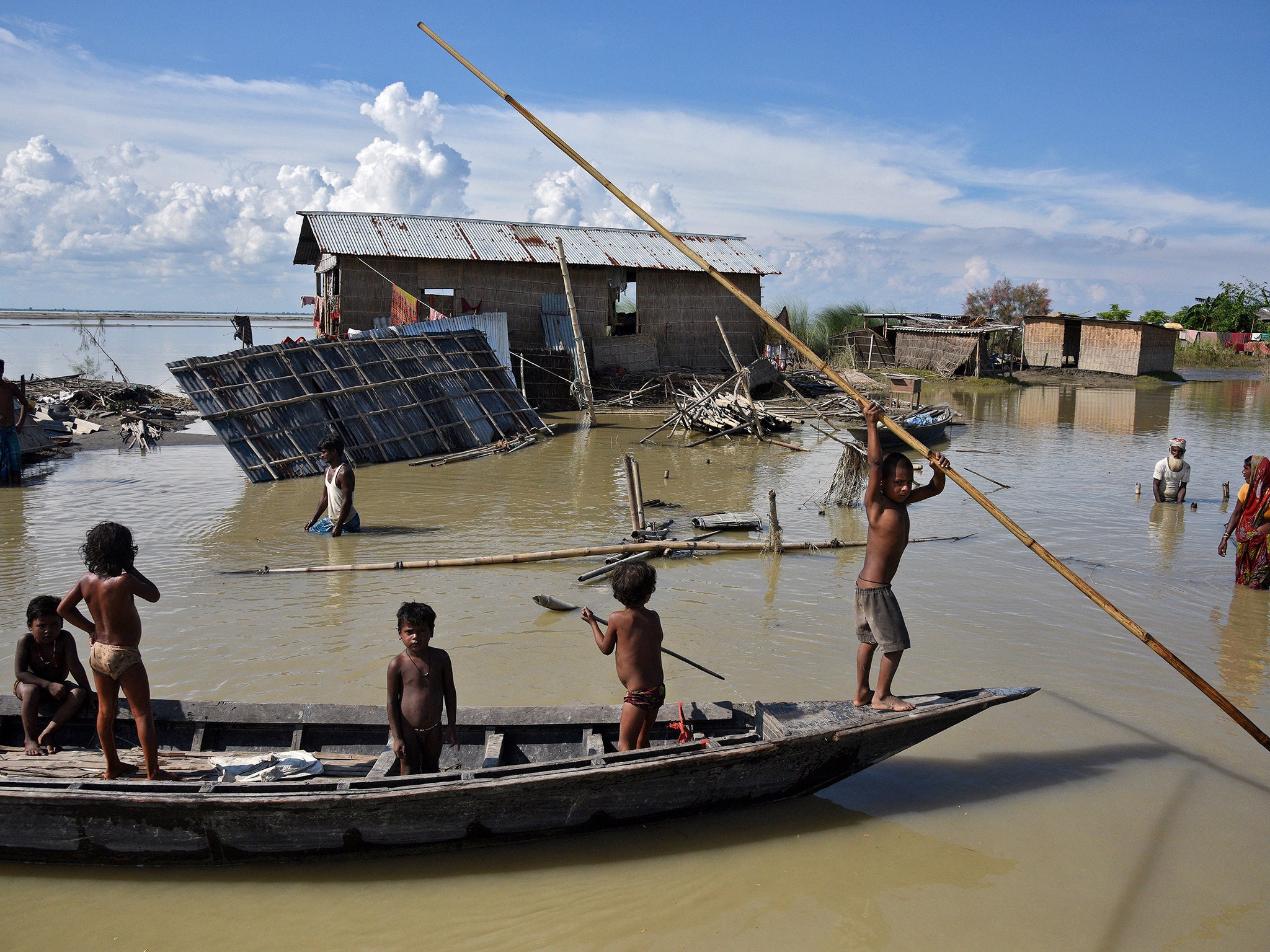 Children row a boat as they pass through damaged houses at a flood-affected village in Morigaon district in the northeastern state of Assam, India.