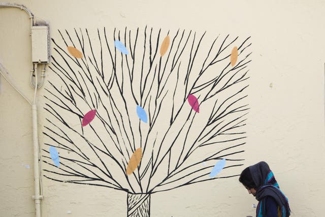 An woman checks her mobile phone as she walks past graffiti of a tree in central Tehran in this file photo from 31 December 2014