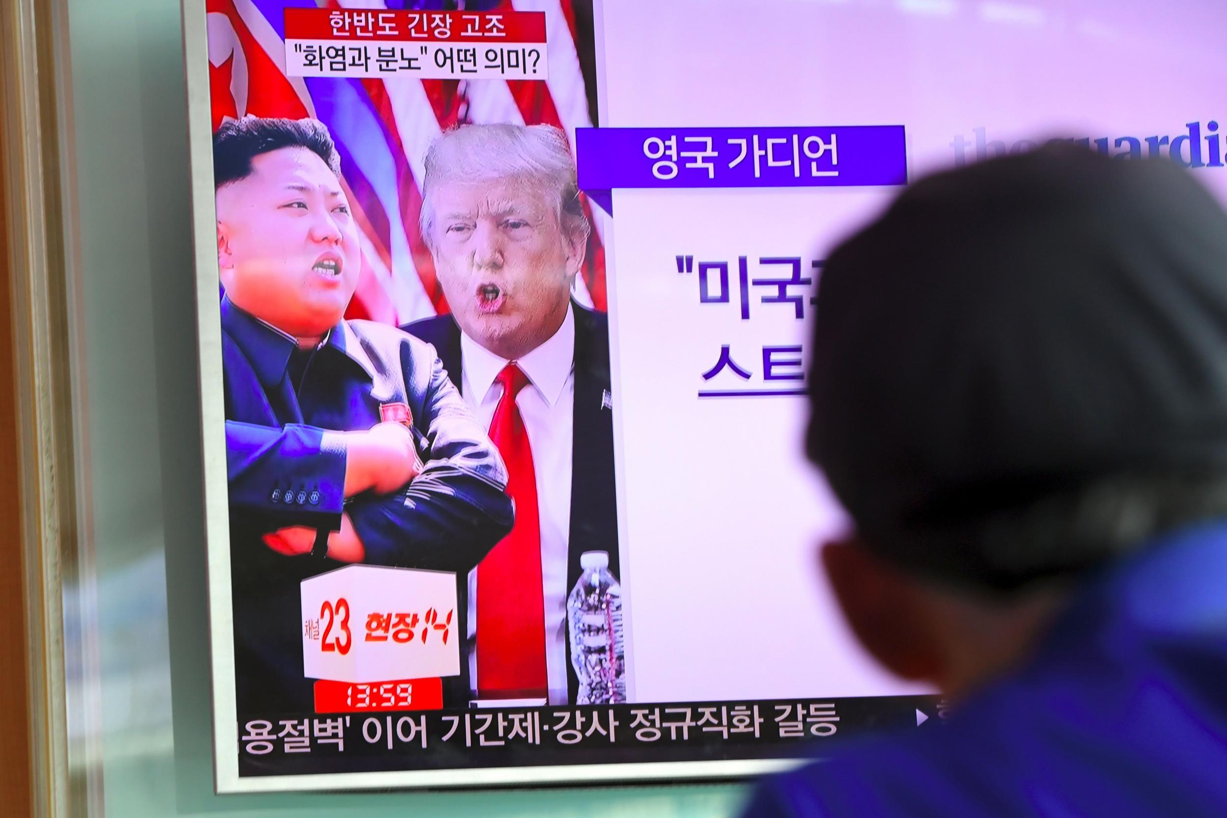 A man watches a television news programme showing US President Donald Trump and North Korean leader Kim Jong-Un