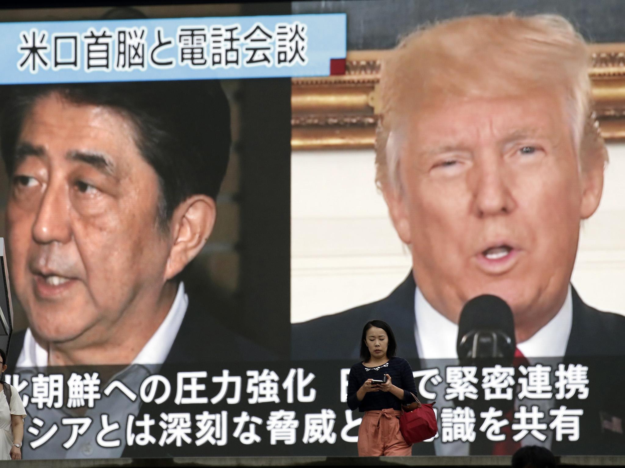 People walk by a TV news program showing the images of Japanese Prime Minister Shinzo Abe, left, and U.S. President Donald Trump while reporting North Korea's nuclear test, in Tokyo