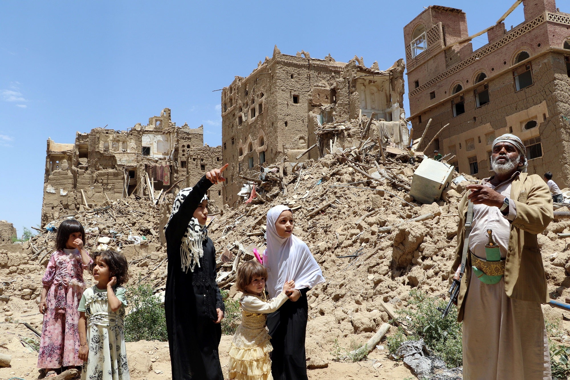 People stand in front of houses destroyed by Saudi-led air strikes in the Yemeni city of Saada