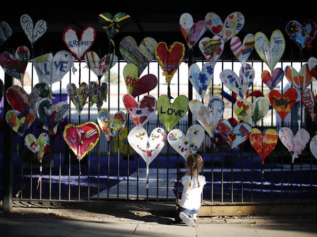 A young girl adds finishing touches to paper hearts adorning a fence in Kensington, near the burnt-out remains of Grenfell Tower