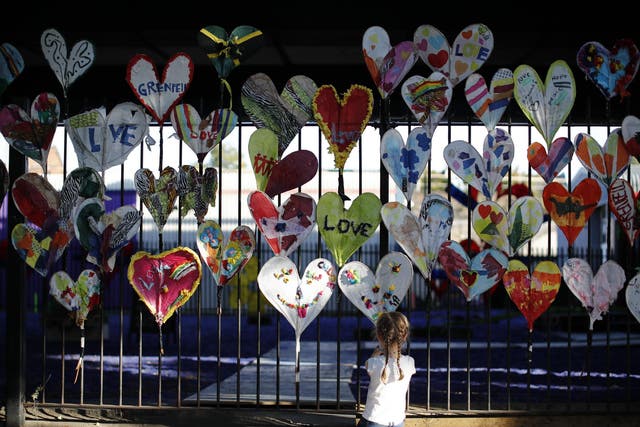 A young girl adds finishing touches to paper hearts adorning a fence in Kensington, near the burnt-out remains of Grenfell Tower