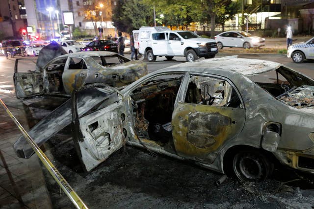 The burned out remains of two taxis are seen behind a police cordon after clashes broke out between metered taxi drivers and Uber taxi drivers this week in the northern suburb of Sandton