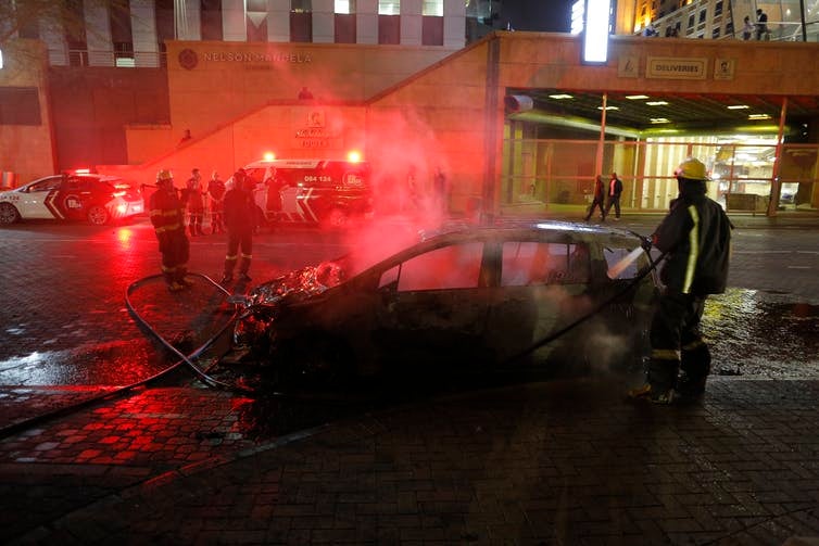 A fireman extinguishes a burned out taxi after clashes broke out between metered taxi drivers and Uber taxi drivers in Sandton City, Johannesberg