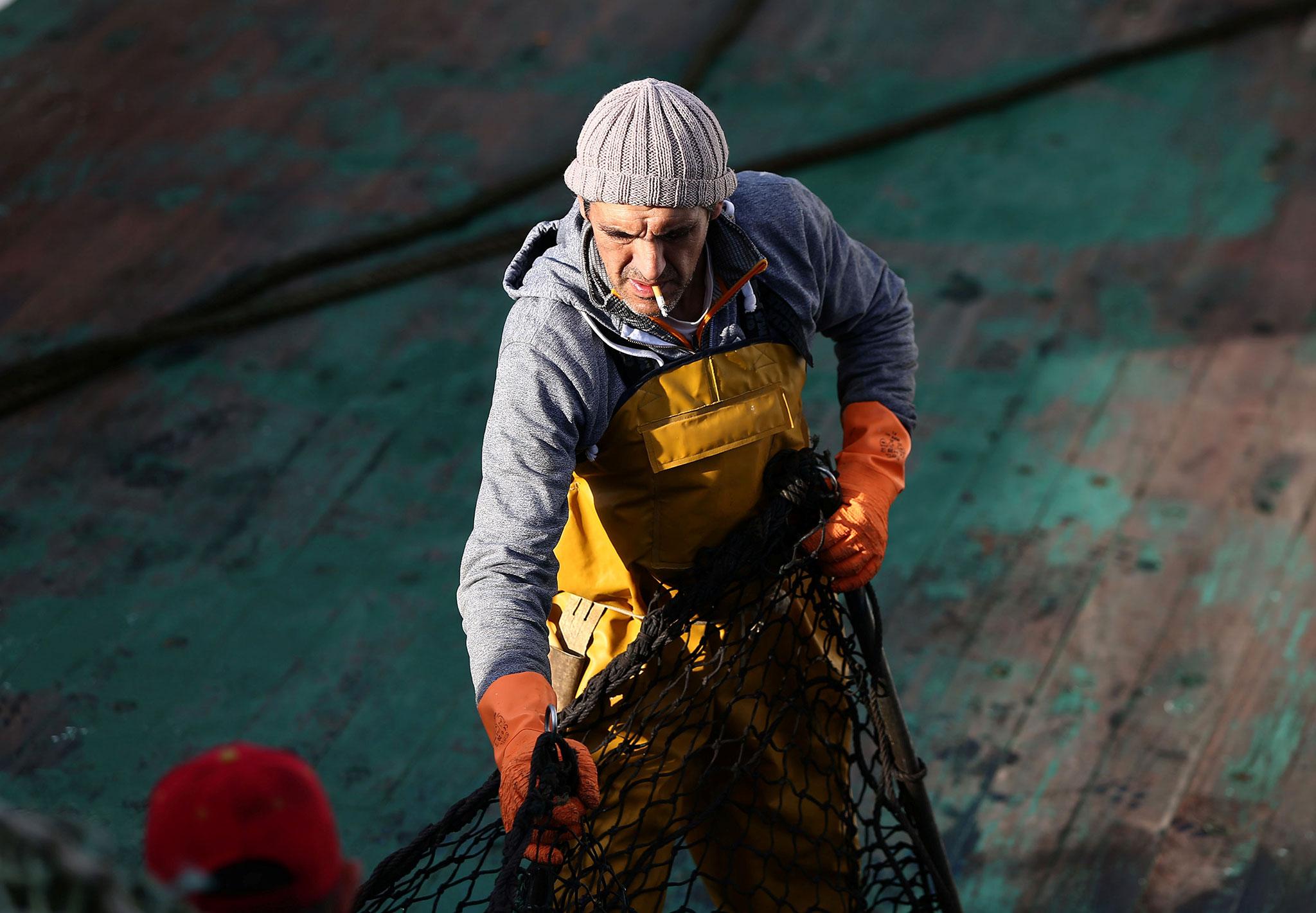 A worker on a fishing vessel pulls a net at a port in Newlyn