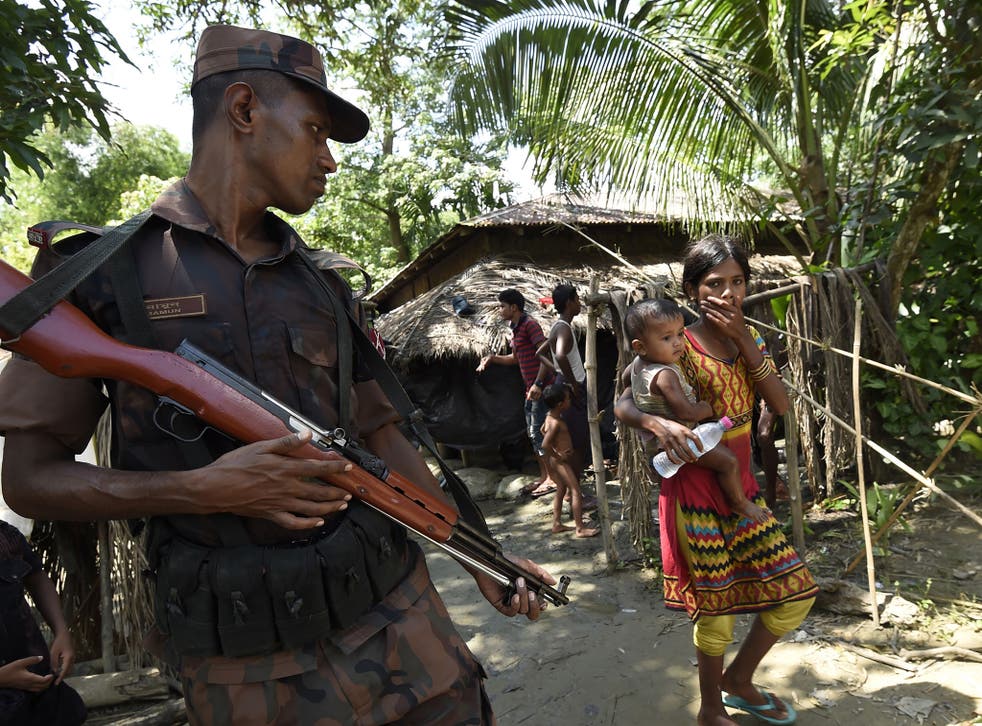 Refugees pass a Bangladeshi border guard at a camp in the no-man's land area between Burma and Bangladesh, near Gumdhum village in Ukhia