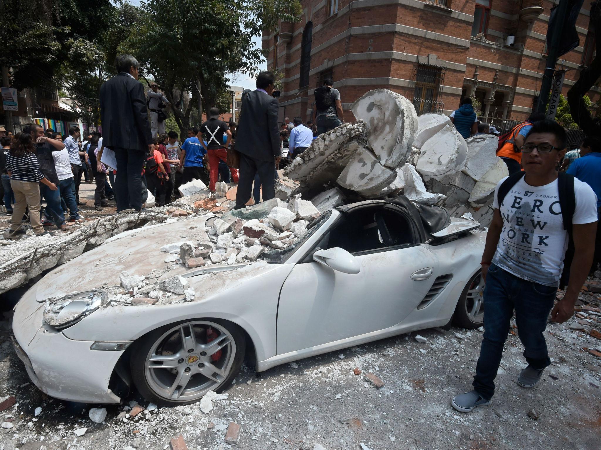 A man stands next to a car crashed by debris from a damaged building after a quake rattled Mexico City on September 19, 2017