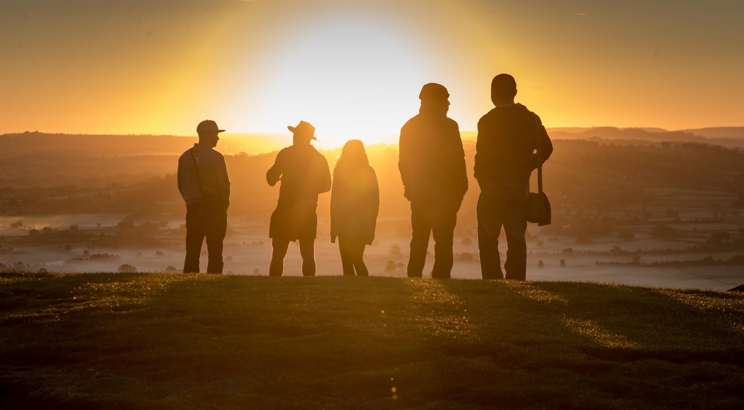 People watch as the autumn sun rises over the Somerset Levels viewed from Glastonbury Tor near Glastonbury
