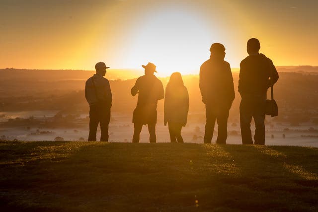 People watch as the autumn sun rises over the Somerset Levels viewed from Glastonbury Tor near Glastonbury