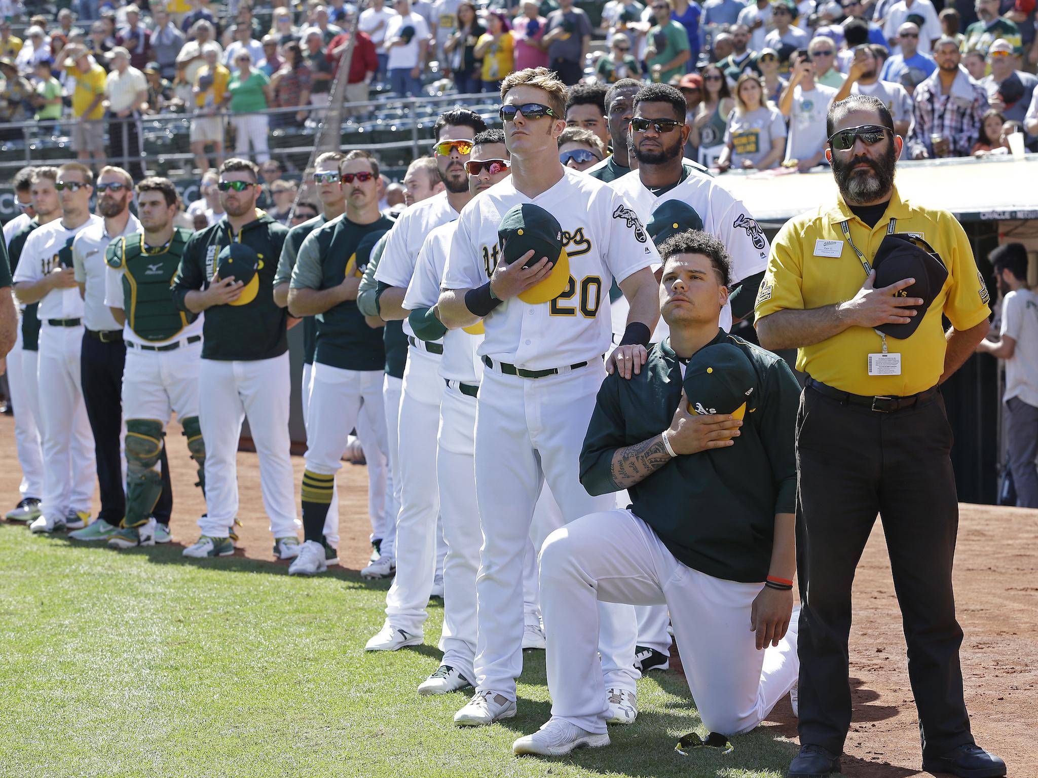 Oakland Athletics' Mark Canha (20) places his hand on the shoulder of Bruce Maxwell as Maxwell takes a knee during the national anthem prior to a baseball game against the Texas Rangers