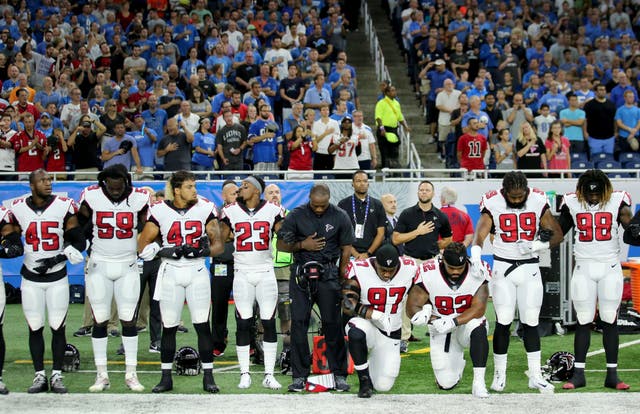 Members of the Atlanta Falcons football team Grady Jarrett and Dontari Poe take a knee during the national anthem while their fellow teammates link arms in solidarity