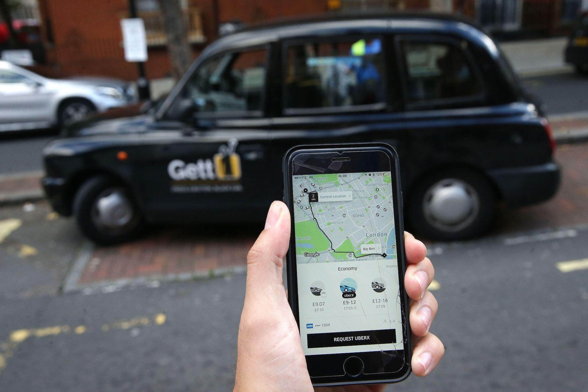 A woman poses holding a smartphone showing the App for ride-sharing cab service Uber in London on September 22, 2017