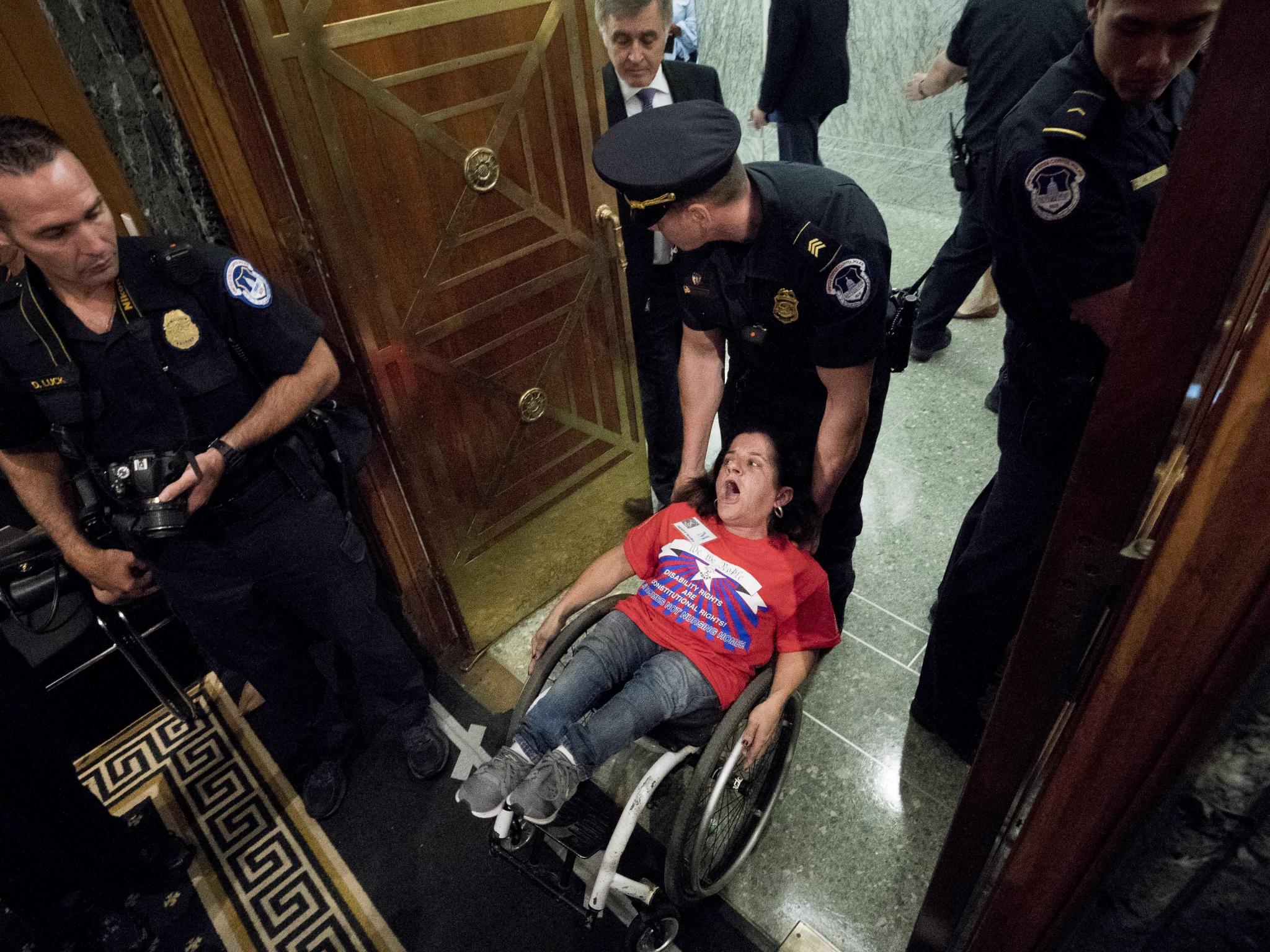A woman in a wheelchair is removed after disrupting a Senate Finance Committee hearing to consider the Graham-Cassidy healthcare proposal on Capitol Hill on 25 September