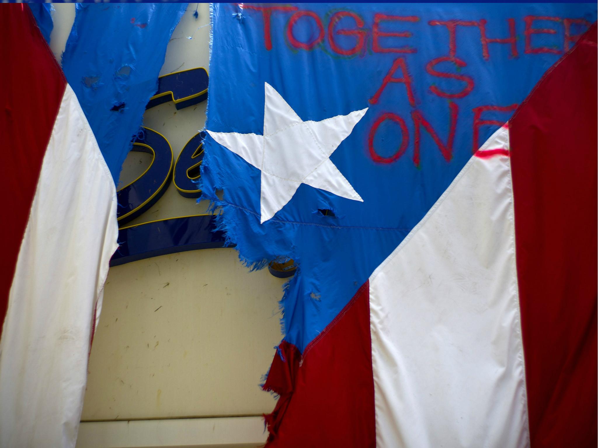 A damaged Puerto Rican national flag spray painted with words "Together as One" hangs from the facade of a business, in San Juan, Puerto Rico on 27 September.