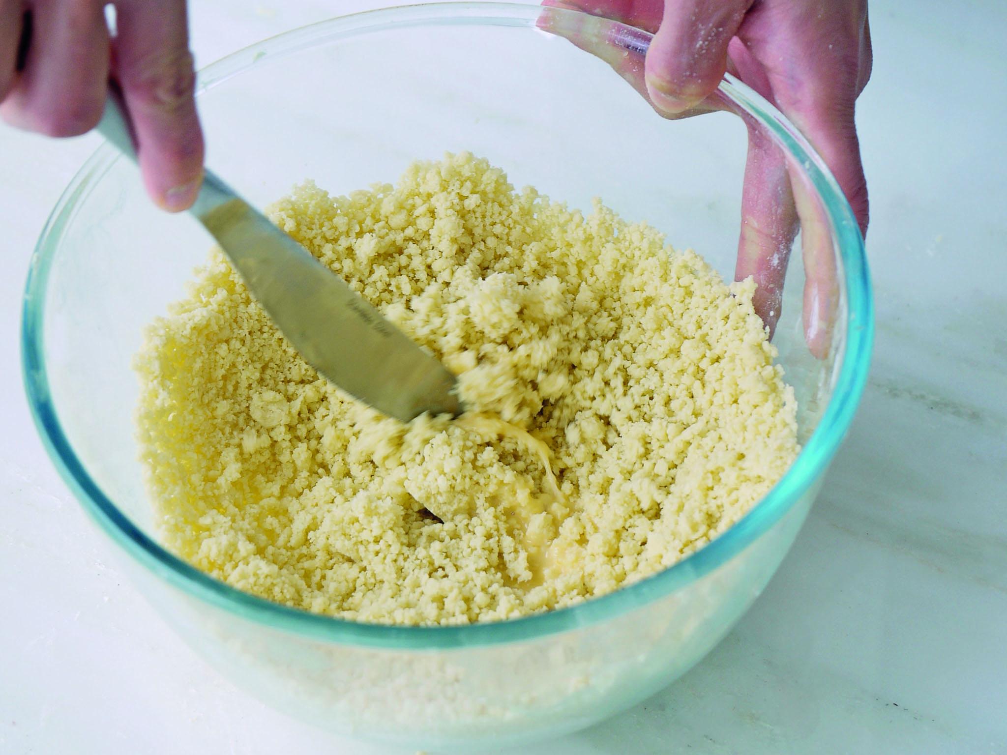 7. Use the flat of the knife to bring a few of the flakes and dry crumb together, to create larger lumps. At this stage, the pastry should be uniform in colour, not streaky. Continue like this until there are no dry crumbs in the bottom of the bowl