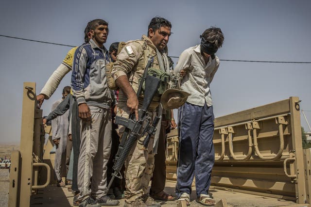 A Kurdish peshmerga soldier hands over a man suspected of being a member of Isis at a screening centre for displaced people near Kirkuk, Iraq, on 1 October 2017