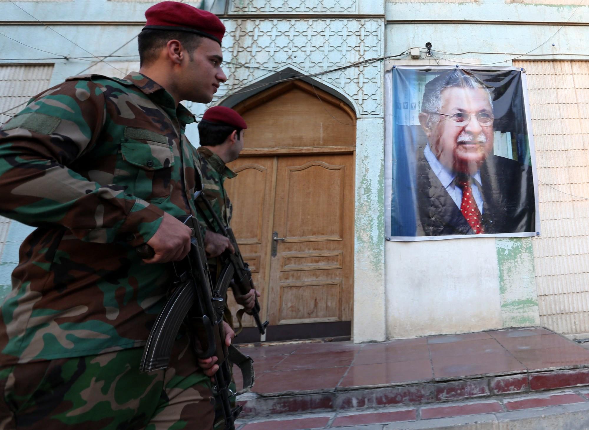Members of the Iraqi Kurdish Peshmerga forces stand guard near the image of former Iraqi President Jalal al-Talabani