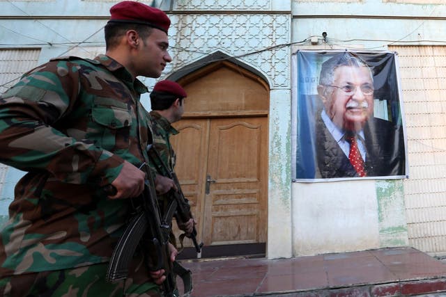 Members of the Iraqi Kurdish Peshmerga forces stand guard near the image of former Iraqi President Jalal al-Talabani
