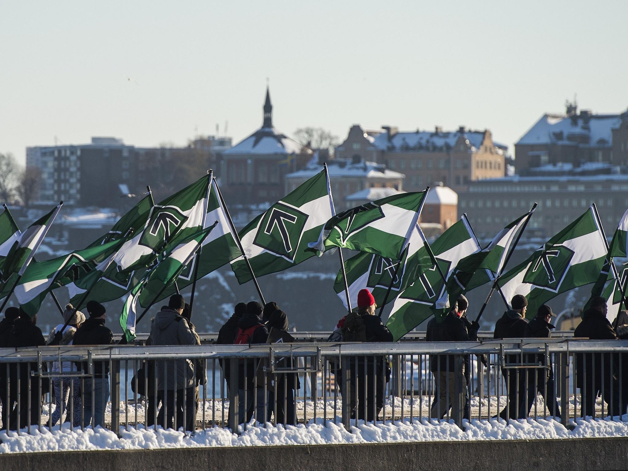 Nordic Resistance Movement supporters marching with flags bearing their 'Tyr rune' logo