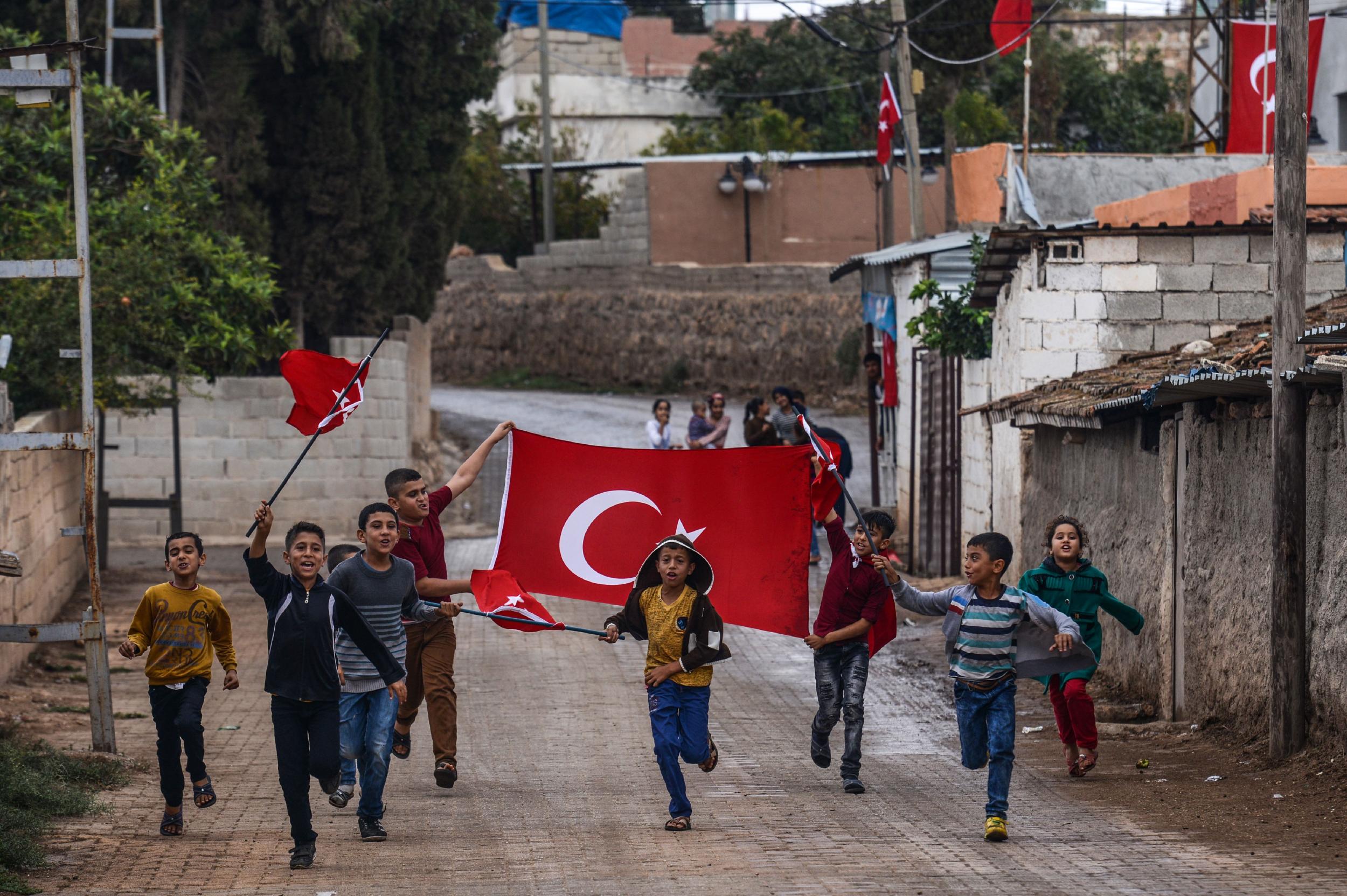 Turkish children run with national flags as they gesture towards army vehicles near the Turkey-Syria border in Reyhanli, Hatay province, on 9 October 2017