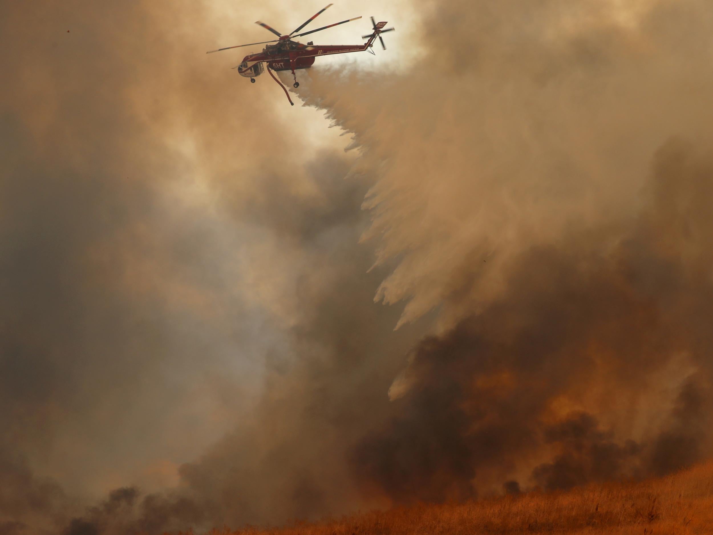 A helicopter drops water on a wind-driven wildfire in Orange, California