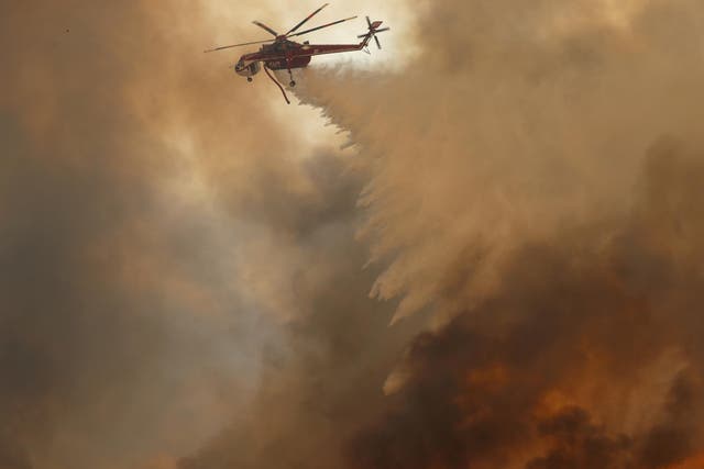 A helicopter drops water on a wind-driven wildfire in Orange, California