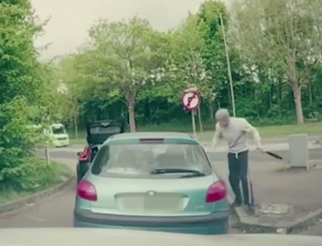 One of the thugs approaches the man's car window with a baseball bat