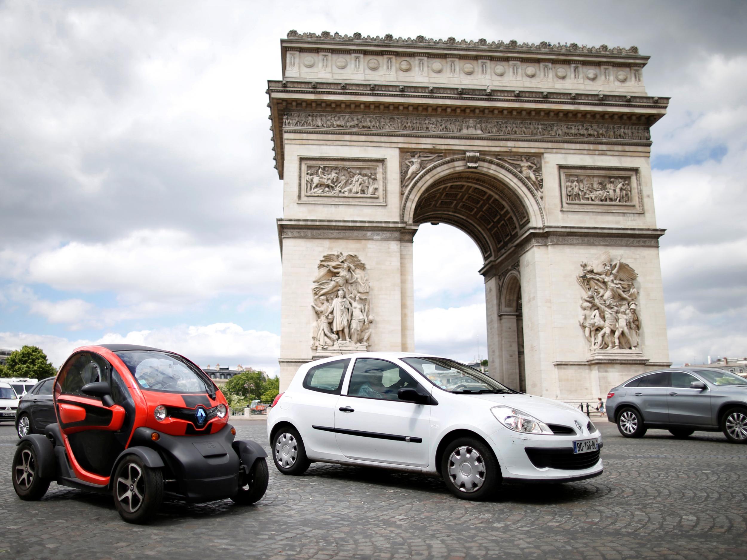 A Renault Clio III and a Twizy electric car drive past the Arc de Triomphe in Paris