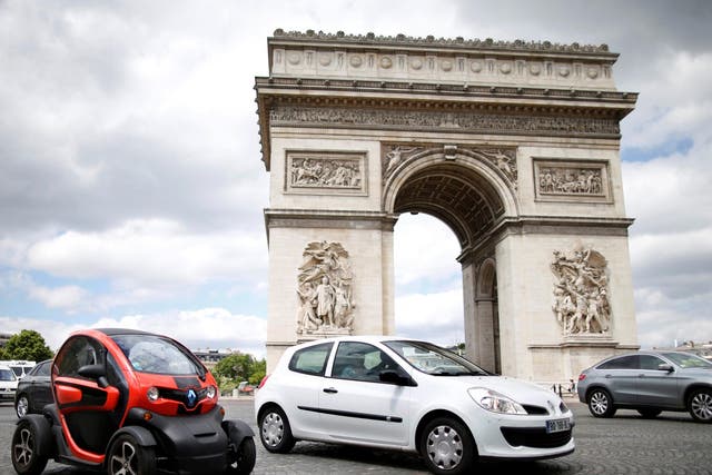 A Renault Clio III and a Twizy electric car drive past the Arc de Triomphe in Paris