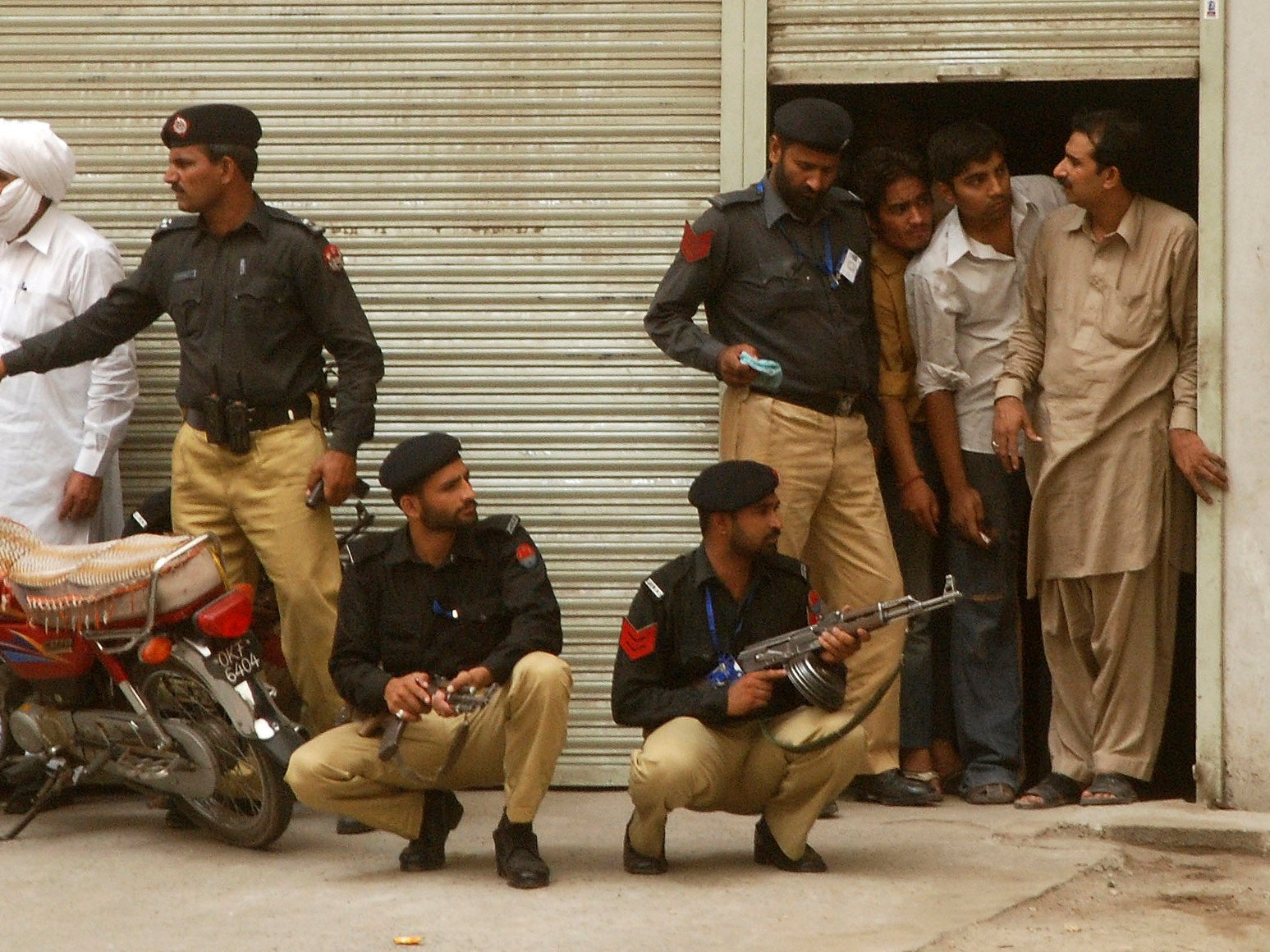 Shop keepers in Lahore's Garhi Shahu neighborhood look past policemen who arrived after gunmen attacked an Ahmadi mosque in the area