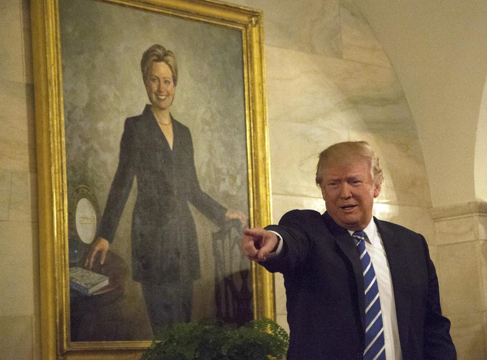 US President Donald Trump walks in a corridor of the White House to greet visitors, while a portrait of Hillary Clinton hangs on the wall, March 7, 2017 in Washington, DC