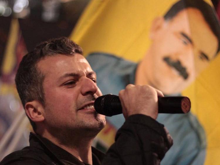 Mehmet speaking at a rally in London, with a poster of his hero Abdullah Ocalan, a Kurdish leader, in the distance
