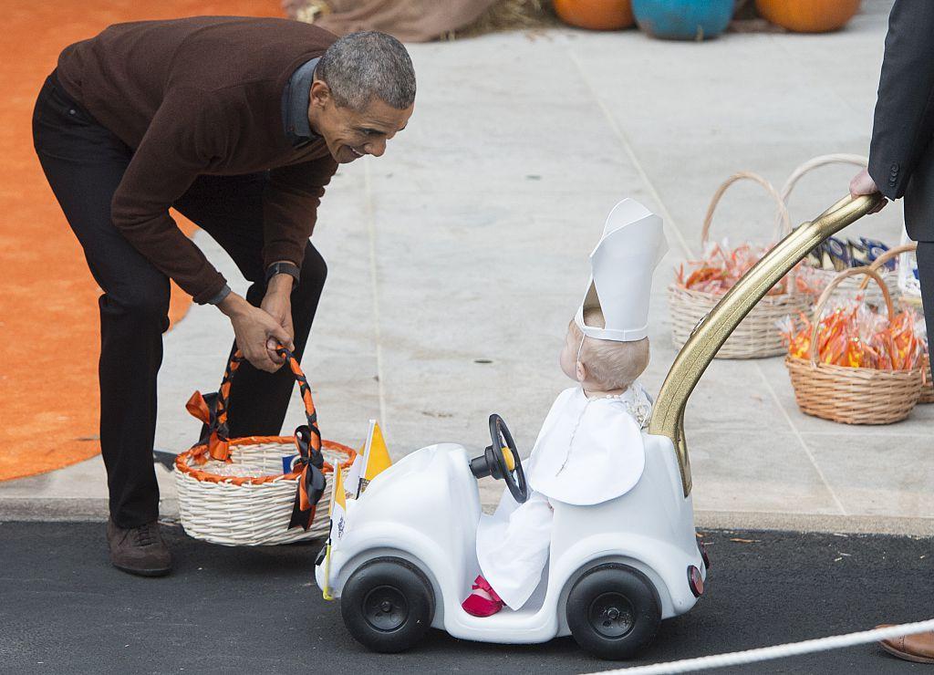 Former US President Barack Obama greets a young child dressed as the Pope as he hands out treats to children trick-or-treating for Halloween