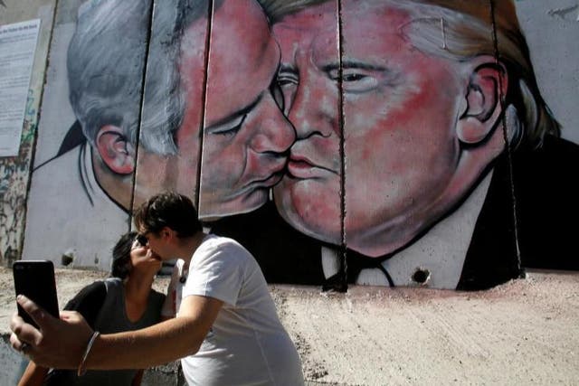 Tourists kiss each other as they stand in front of a mural depicting US President Donald Trump and Israel's Prime Minister Benjamin Netanyahu kissing each other in the West Bank city of Bethlehem