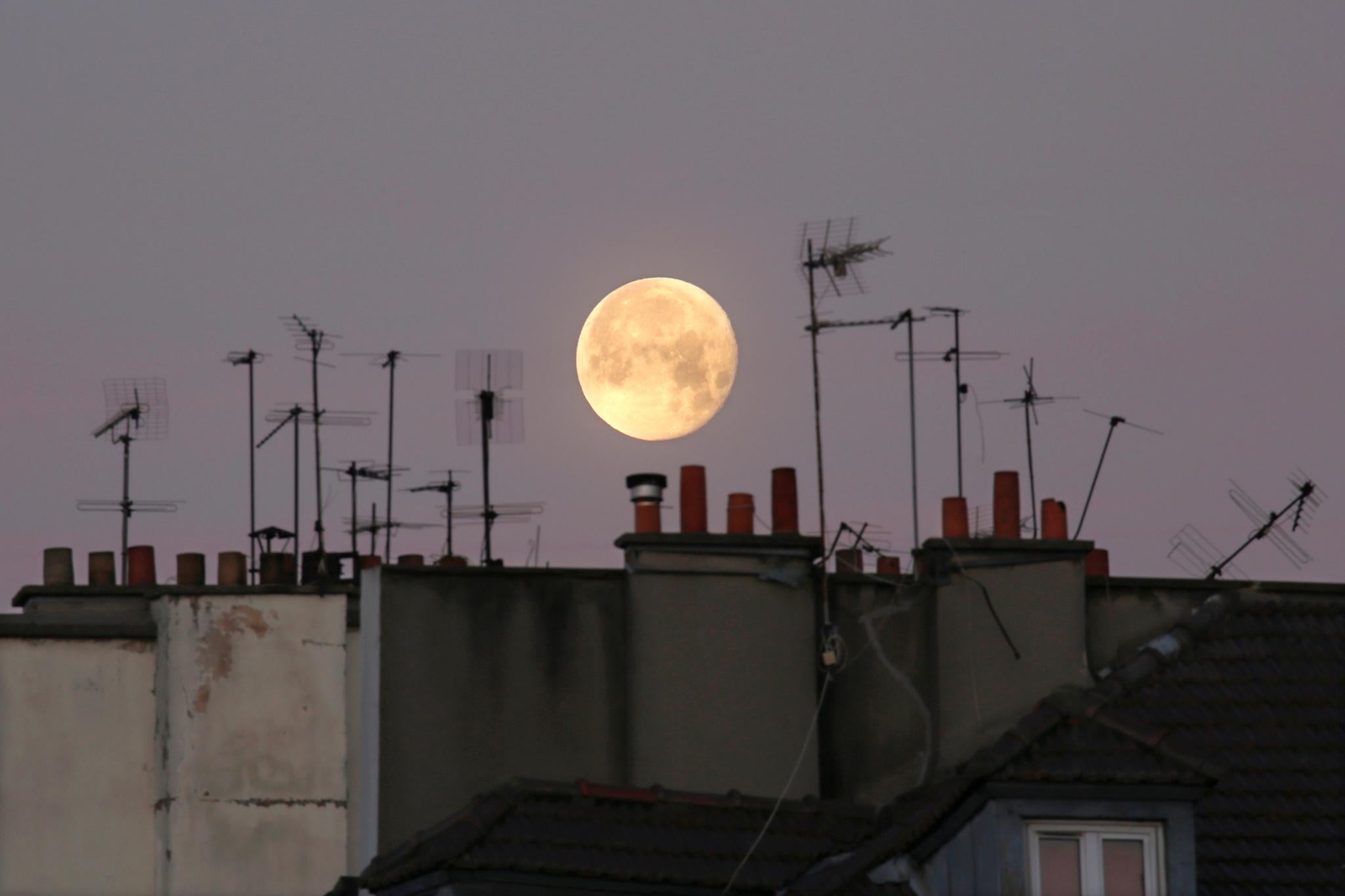 The moon is seen behind chimneys and tv antennas stacked on the rooftops of residential buildings in Paris, France, December 15, 2016