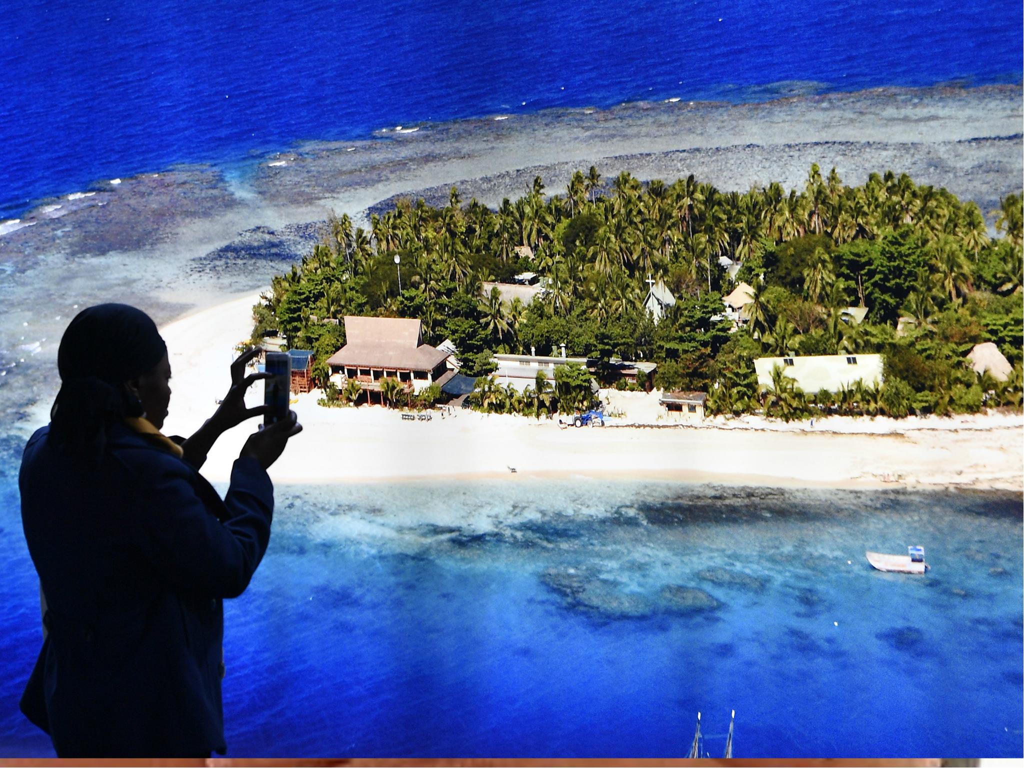 A delegate takes a picture in front of a photo of an island at the COP 23 Fiji UN Climate Change Conference in Bonn, 6 November 2017.