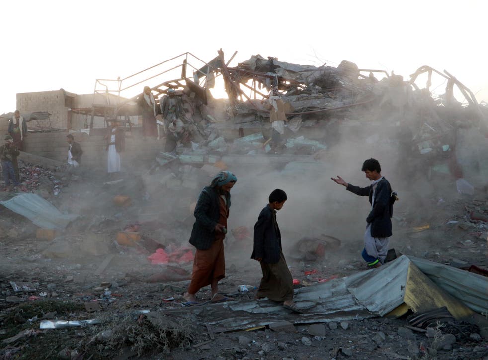 People walk at the site of an air strike in the north western city of Saada, Yemen