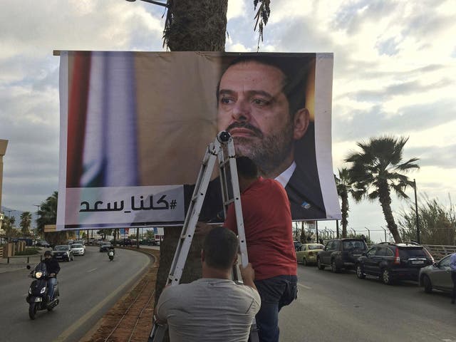 Workers in Beirut hang a poster of outgoing Prime Minister Saad Hariri with Arabic words that read, 'We are all Saad'