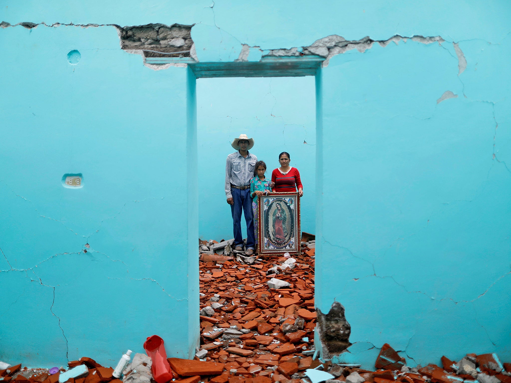 Luis Medina, Maria Teresa Espinoza, and Maria de Jesus Medina inside their house which was badly damaged. They are living in their backyard as they wait for their home to be demolished and rebuilt.
