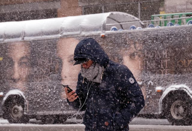 A man uses his smartphone as he crosses a street during a winter storm in New York on March 5, 2015