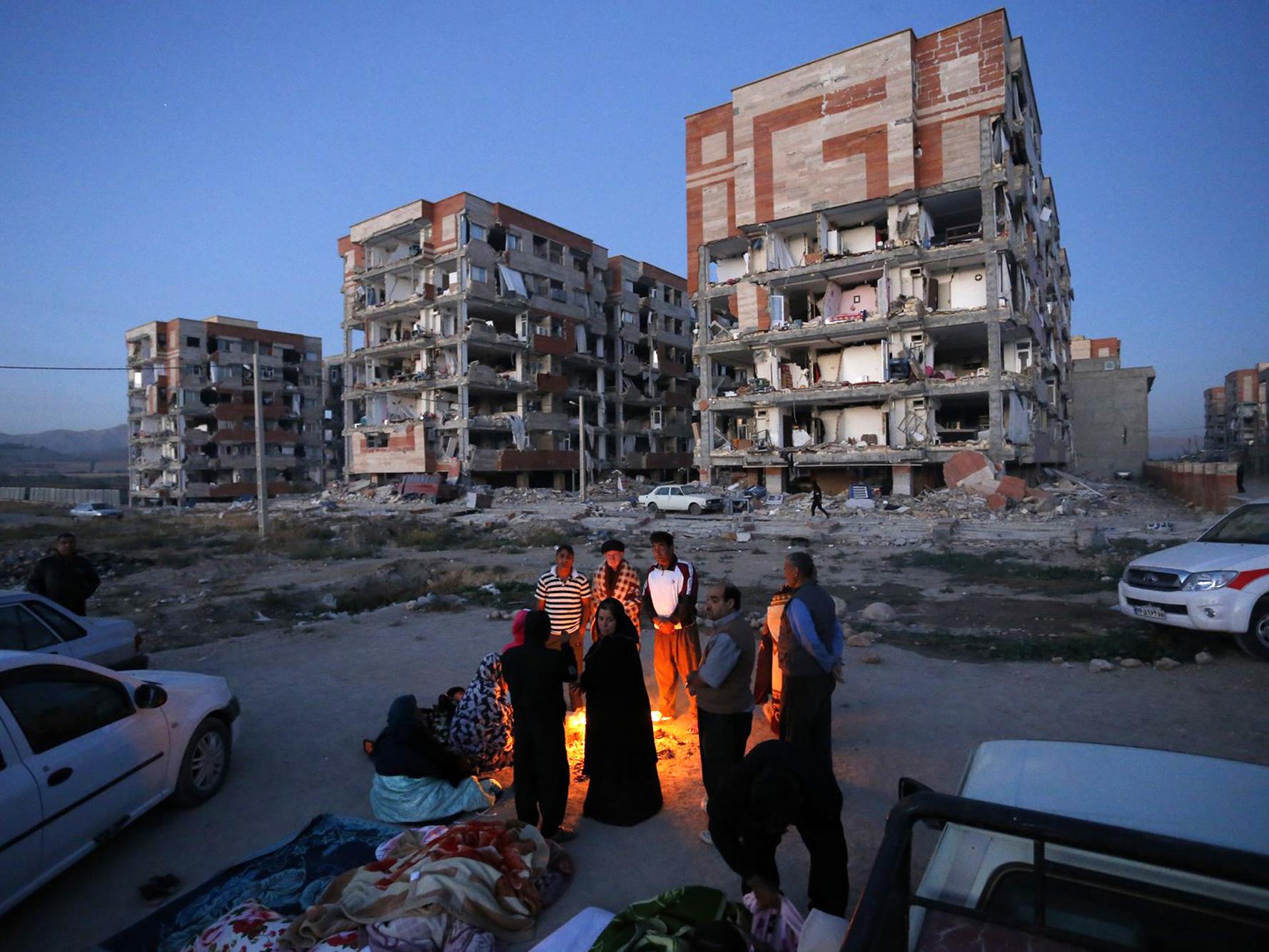 Survivors of the earthquake warm themselves in front of destroyed buildings at the city of Sarpol-e-Zahab in western Iran