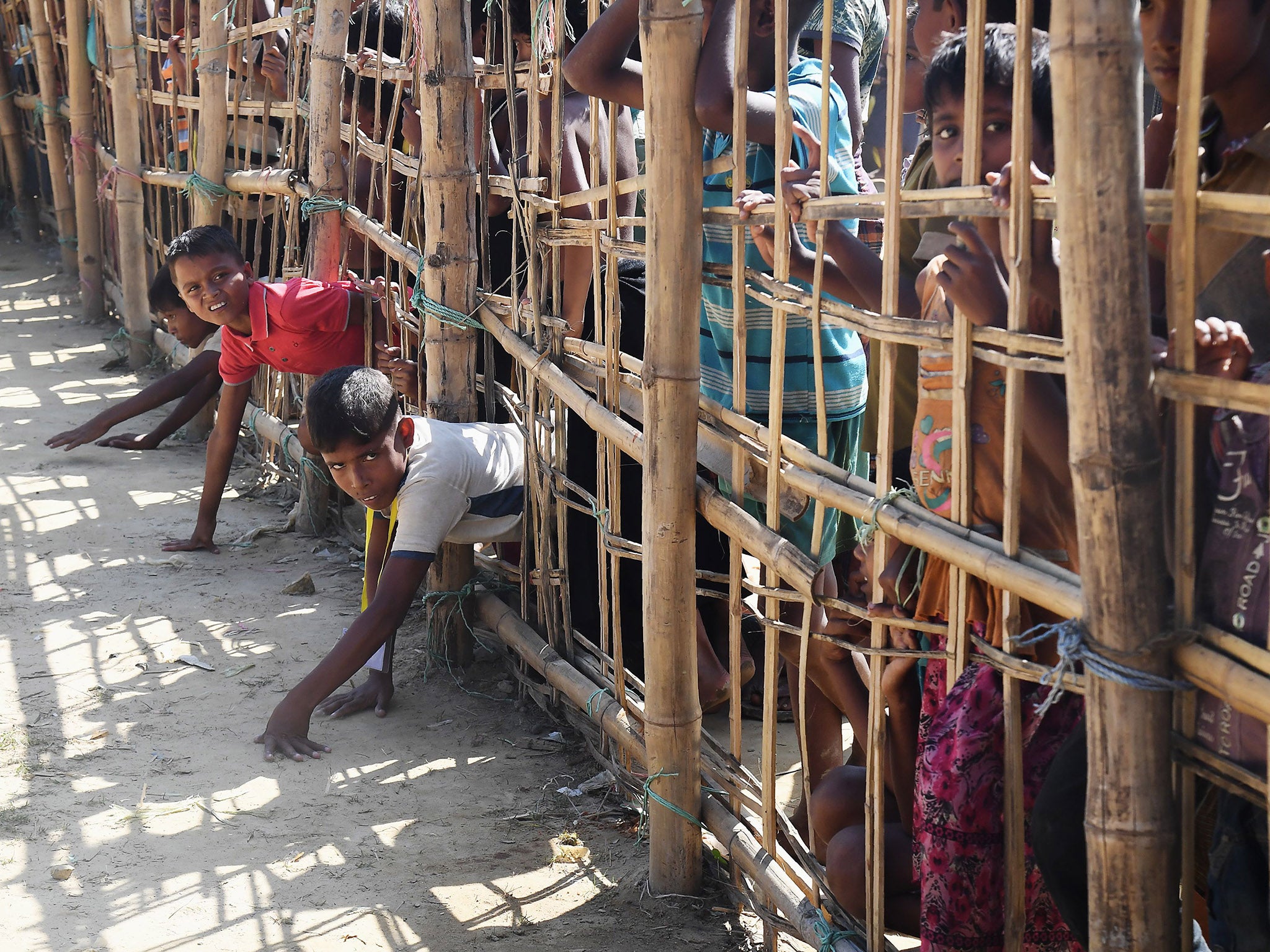 Young Rohingya refugees trying to climb through a temporary bamboo fence as they try to collect food at a camp in Bangladesh