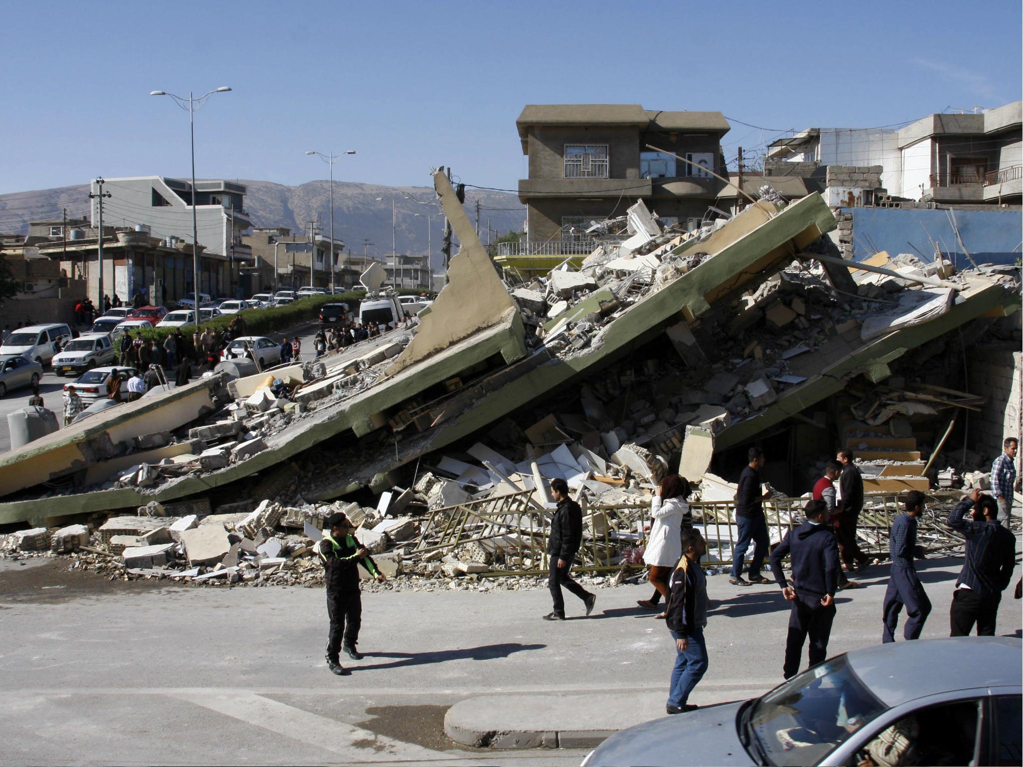 People gather around a levelled building in the mountainous town of Darbandikhan in Iraqi Kurdistan on 13 November 2017, following a 7.3-magnitude earthquake.