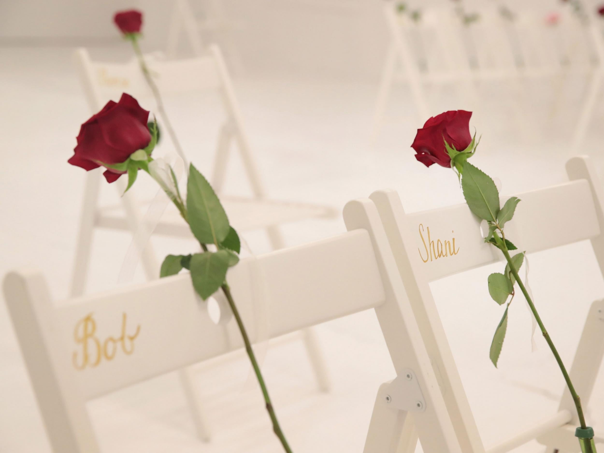 On each chair is a single rose and the name of a shooting victim